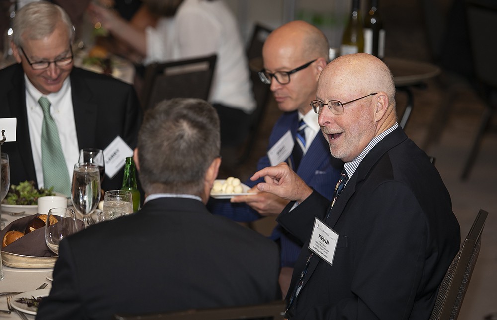 Medical Device Industry Supply Chain Council’s Kevin Stout chats with Bellwether League’s Mark Van Sumeren (back to camera) with Eric O’Daffer and Larry Smith (Bellwether Class of 2019) in the background to his right.