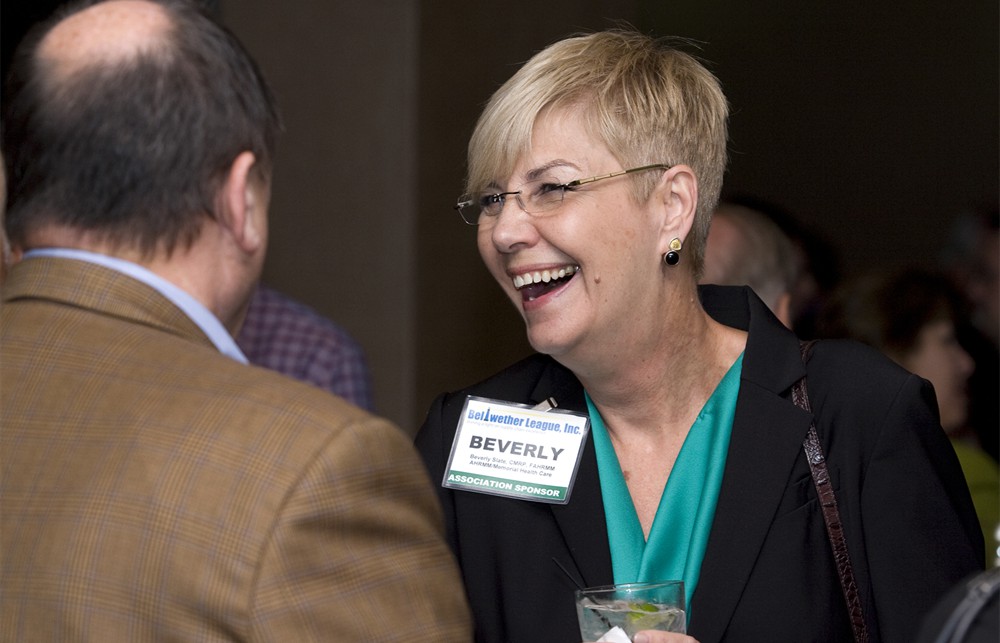 AHRMM President Bev Slate laughs with Defense Health Support Systems’ Bob Perry (left, back to camera), an AHRMM past president