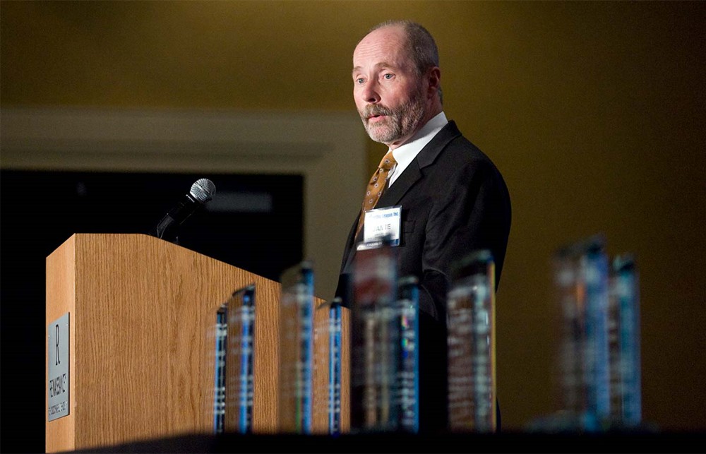 Co-Founder and Chairman Jamie Kowalski addresses attendees as the Beacon awards await their recipients (foreground).